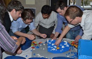Peo-ple gathered around a table full of lego taking part in a team activity - How to plan a team building event