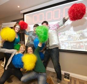 A group of 5 people with Pom Poms taking part in team building activities for large groups.