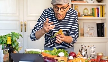Man in a stripey t-shirt cooking food whilst watching a laptop